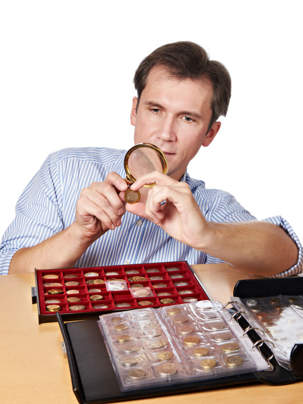 Man numismatist examines  coin with magnifying glass